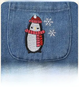 Detailed close-up of 3D penguin embroidery and snowflakes on blue denim dress fabric