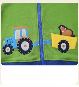 Détail de la broderie bouclée d'un tracteur jaune et d'une vache sur un sweat enfant