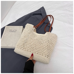 Detail view of a beige woven tote bag with hollow texture and brown leather handles