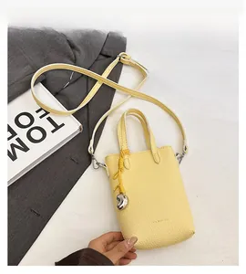 Détail du mini sac bandoulière en cuir litchi jaune avec breloque cœur et poignée haute