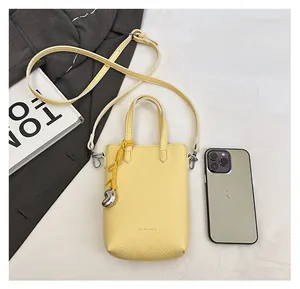 Petit sac bandoulière jaune pâle en cuir à côté d'un smartphone montrant sa capacité
