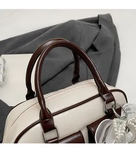 Close-up of contrast leather Boston bag with round handles and pearl bow charm
