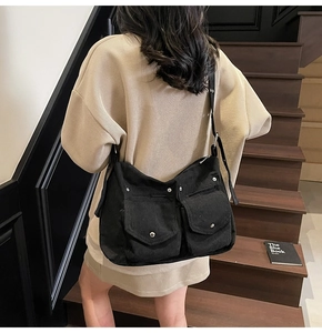 Détail du sac bandoulière en toile noire avec poches cargo et rivets argentés