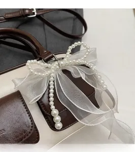 Close-up of elegant white organza bow charm with pearls on a leather Boston bag handle