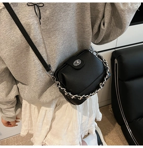 Detail of black lychee grain leather crossbody bag with silver chain and metal turn lock
