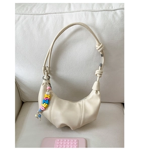 Close-up of a cream croissant shoulder bag with knot detail and colorful letter charms