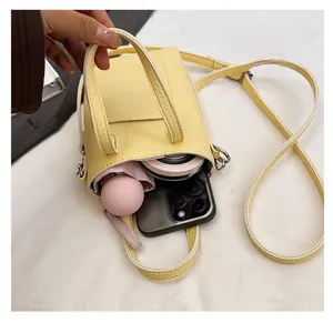 Intérieur du mini sac en cuir jaune contenant smartphone, poudrier et parapluie de soleil