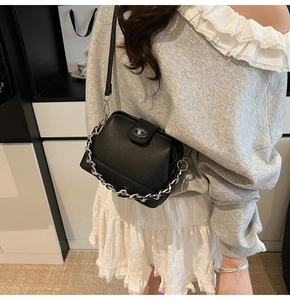Close-up of black litchi leather bucket bag with silver chain and metal lock on model