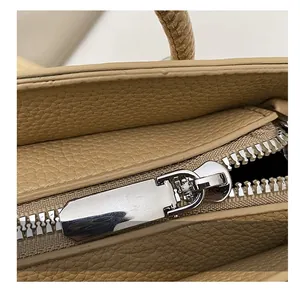Detailed macro view of the silver metal zipper on a light khaki lychee grain leather bag
