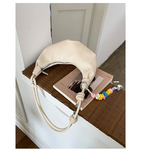 Detail of off-white croissant bag with decorative knotted strap and colorful beads