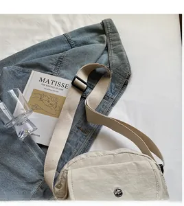 Detailansicht beige Umhängetasche mit breitem Gurt und metallischem Logo vorne