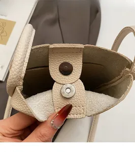 Detail view of beige crossbody bag with magnetic snap closure and lychee texture