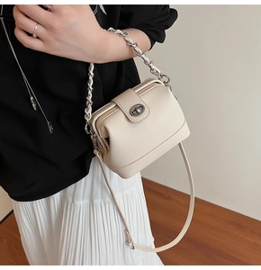 Detail view of beige leather bucket bag with silver chain strap and metal swivel lock
