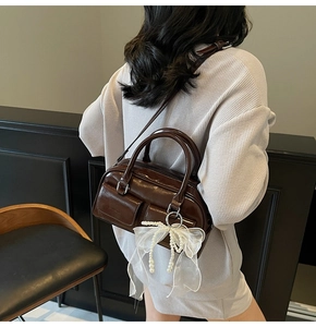 Detail of dark brown glossy Boston bag featuring lace bow charm and pearl strap detail