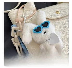 Detail of white plush bunny charm with blue heart glasses on a leather tote bag