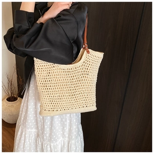 Close-up of cream woven tote bag featuring brown leather handles and knit hollow pattern