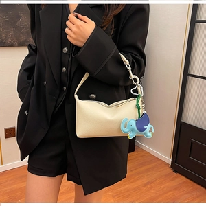 Dettaglio della borsa baguette in pelle crema con ciondolo a elefante blu sulla tracolla