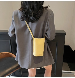 Detail of yellow lychee texture cylinder crossbody bag worn by a model in a grey suit