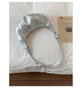 Close-up of silver crescent handbag with pleated texture and knot shoulder strap detail