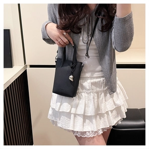Détail du mini sac cabas en cuir grainé noir avec pendentif cœur argenté porté par le mannequin