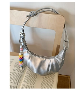 Detail of silver crescent hobo bag with knotted strap and bright bead charm on a book
