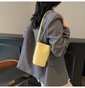 Detail of a bright yellow bucket bag with litchi texture and a slender shoulder strap