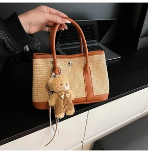 Détail d'un sac cabas en paille avec anses en cuir marron et pendentif ours en peluche