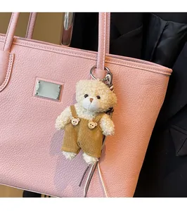 Detail of a fluffy cream bear charm with brown corduroy overalls on a pink tote bag