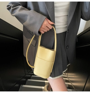 Pale yellow bucket bag in pebble leather carried by model in grey suit at stairs