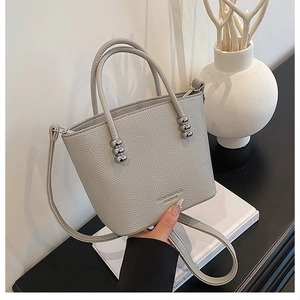 Close-up of grey pebbled leather handbag featuring silver ball hardware and logo detail