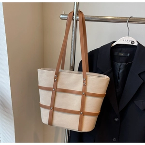 Detail of beige canvas tote with brown leather plaid pattern and silver stud accents