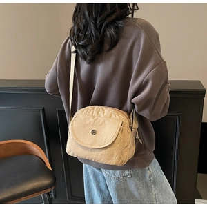 Detailansicht beige Umhängetasche aus Nylon mit Klappe und Logo getragen von einem Modell