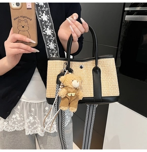 Détail du sac seau en paille avec bordure en cuir noir et pendentif d'ours en peluche