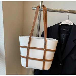 Detail of white canvas tote bag featuring brown leather cross-strap and silver rivets