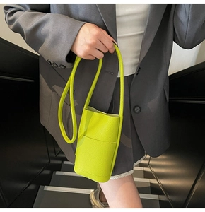 Close-up of neon green pebble leather crossbody phone bag worn with a grey blazer