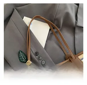 Detail of woven straw tote bag with leaf pendant and brown leather handles on grey fabric