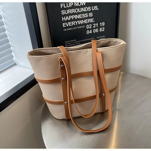 Detail of beige canvas tote bag with brown leather straps and silver studs on metal table