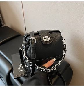 Detail of black pebbled leather bucket bag with silver chain strap and oval twist lock