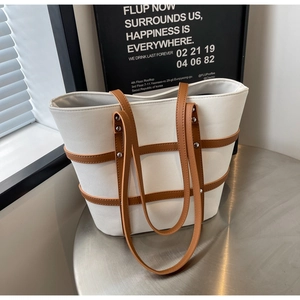 Detail view of large canvas tote bag with brown leather trim and silver metal rivets