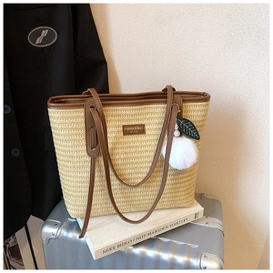 Detail of straw tote bag with leather trim and decorative leaf pompom pendant