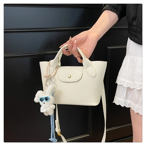Detail of white mini tote bag with lychee texture and cute rabbit plush charm decoration