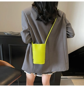 Detail of neon green crossbody phone bag with lychee texture on grey blazer