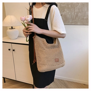 Detail of hand-woven beige crochet tote bag with brown leather tag and long shoulder straps