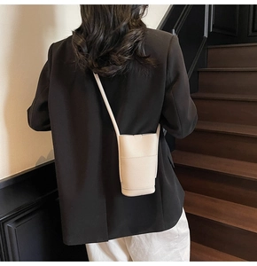 Detail shot of beige textured leather phone crossbody bag worn by a model in a minimalist setting