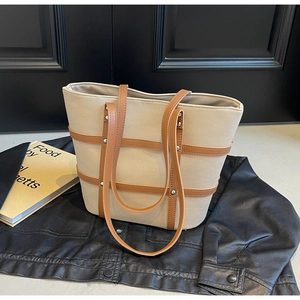 Detail of beige canvas tote with brown leather straps and metal rivets on leather jacket