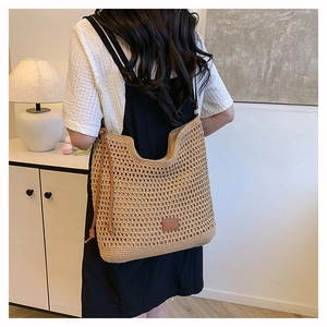 Detail view of large woven tote bag with brown leather strap in a home setting
