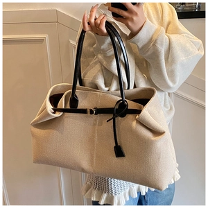 Detail of canvas tote bag showing beige fabric texture, black leather straps and gold buckle