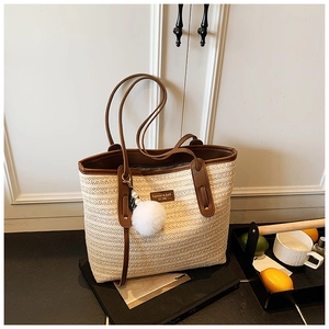 Close-up of bohemian straw tote bag with brown PU leather trim and fuzzy charm detail