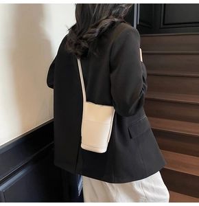 Detail of cream white lychee leather mini bucket bag worn as a crossbody shoulder bag