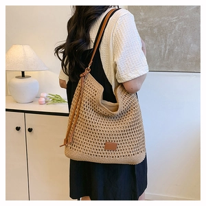 Detail of woven straw tote bag with brown leather straps shown in a warm indoor setting